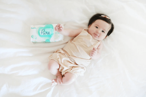 cute baby girl on a bed beside a wet wipes package